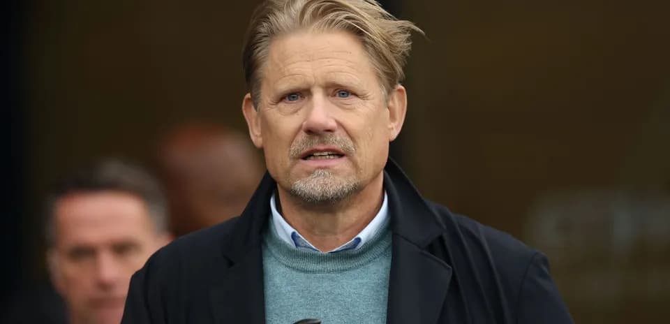 Hombre con abrigo oscuro y suéter gris en evento