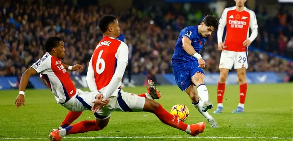 Jugador de Chelsea disparando mientras es tackleado por Arsenal