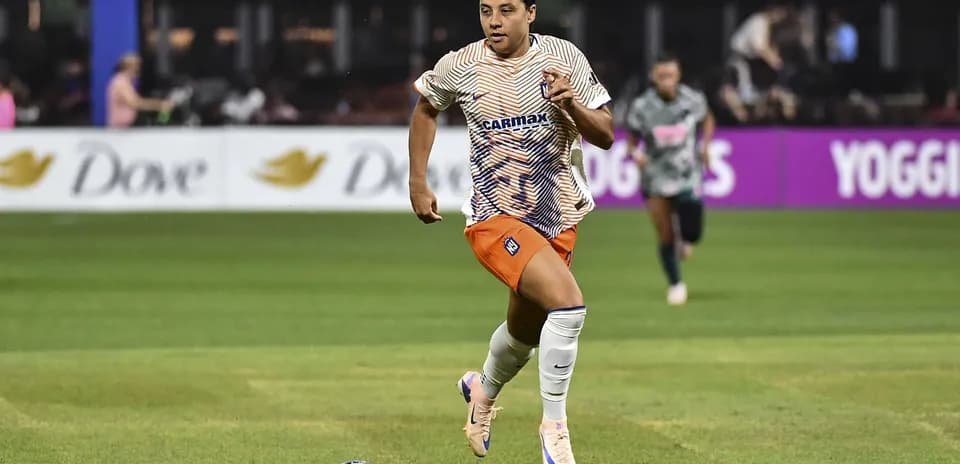 Jugadora corriendo con balón en el campo de fútbol
