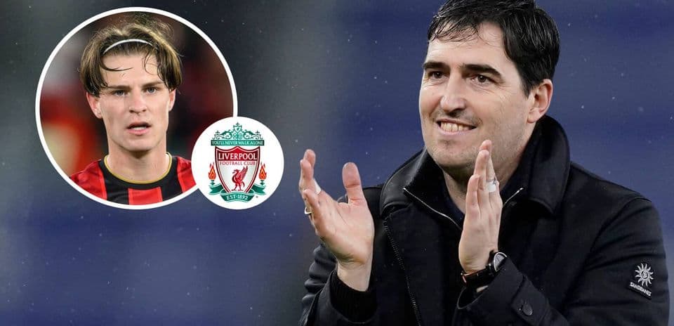 Entrenador aplaudiendo con jugador de fondo y logo de Liverpool