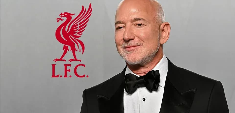Hombre con traje en evento, logo de Liverpool F.C. detrás