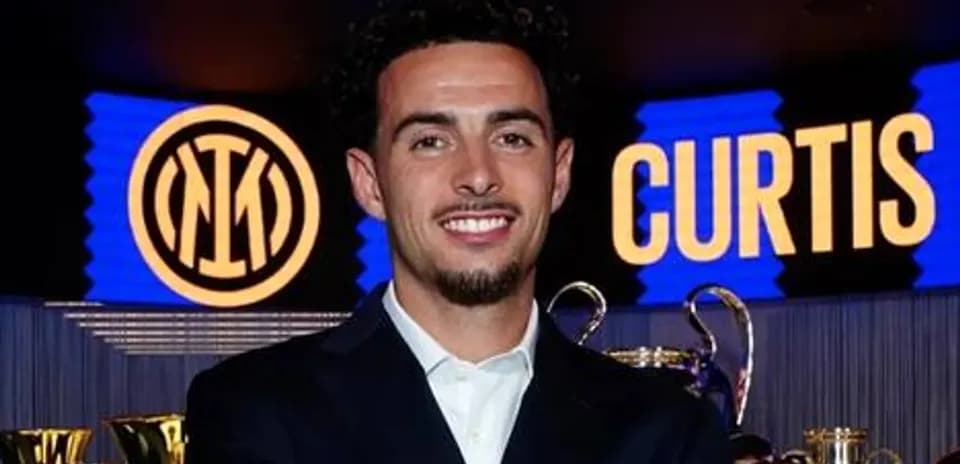 Jugador sonriente en evento con trofeos detrás