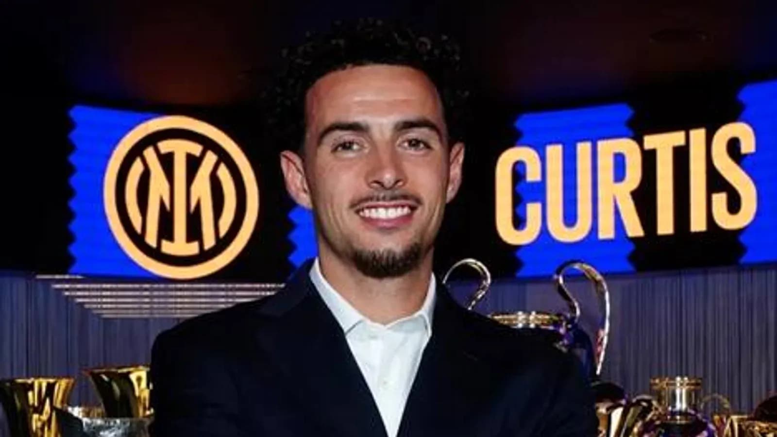 Jugador sonriente en evento con trofeos detrás