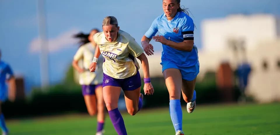 Jugadora de JMU corriendo con balón, perseguida por rival