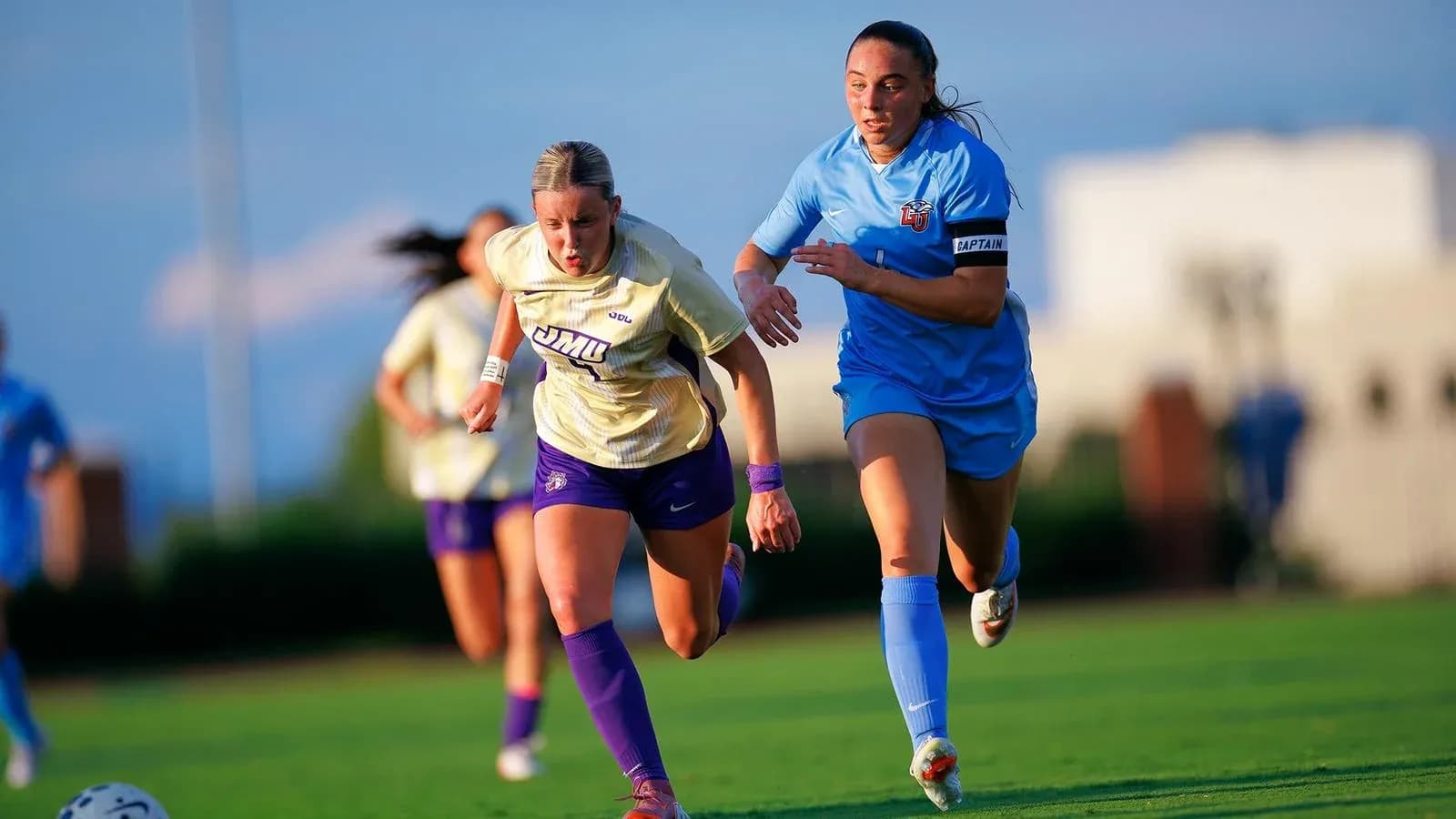 Jugadora de JMU corriendo con balón, perseguida por rival