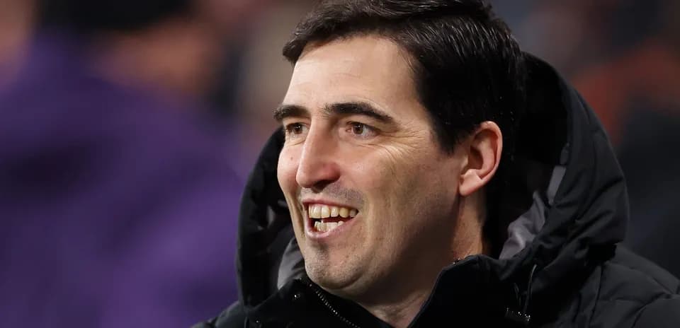 Entrenador sonriendo en el banquillo durante el partido