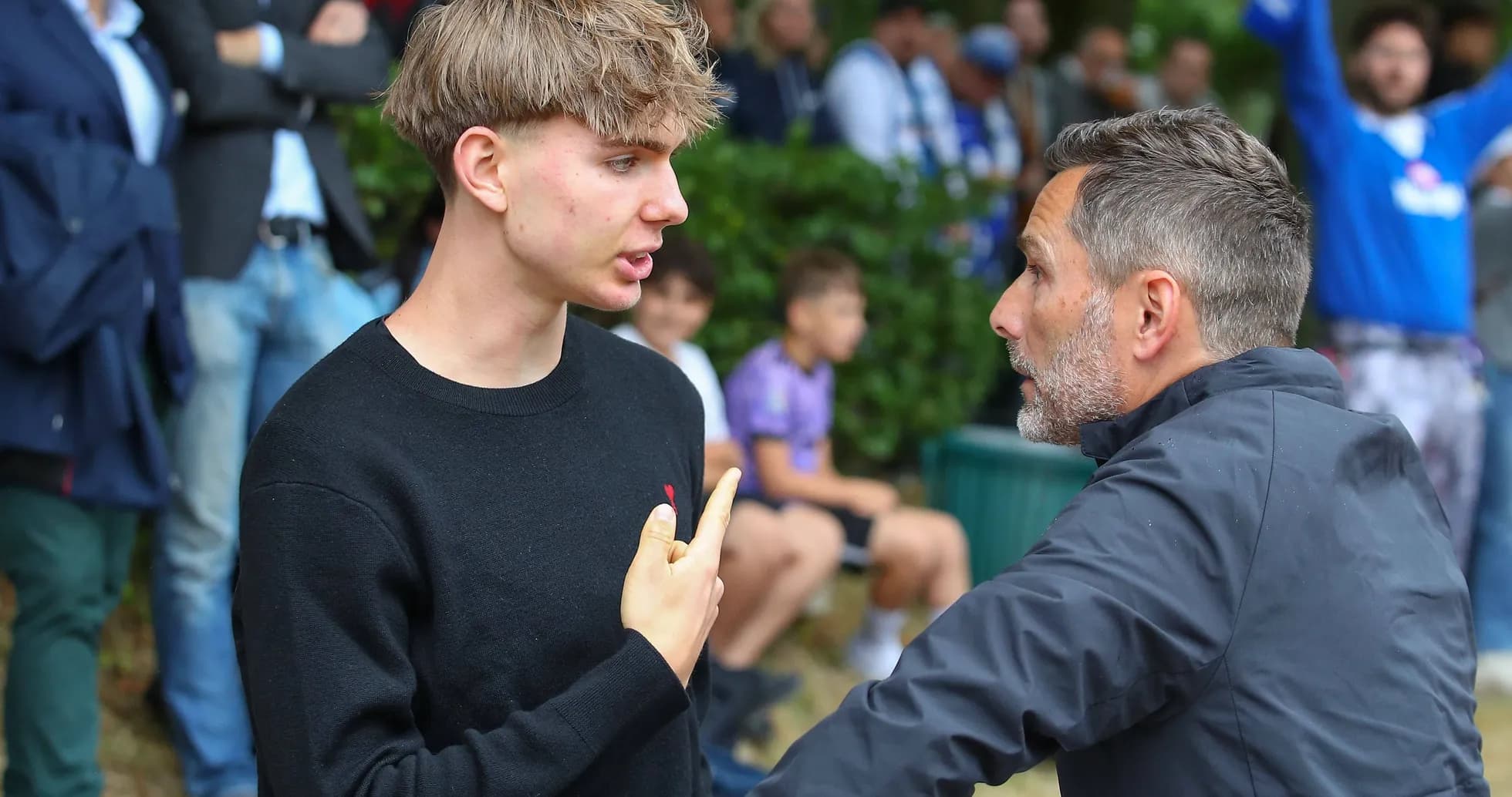 Joven y entrenador conversando en un evento deportivo