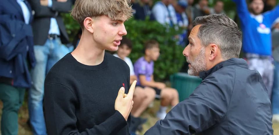 Joven y entrenador conversando en un evento deportivo