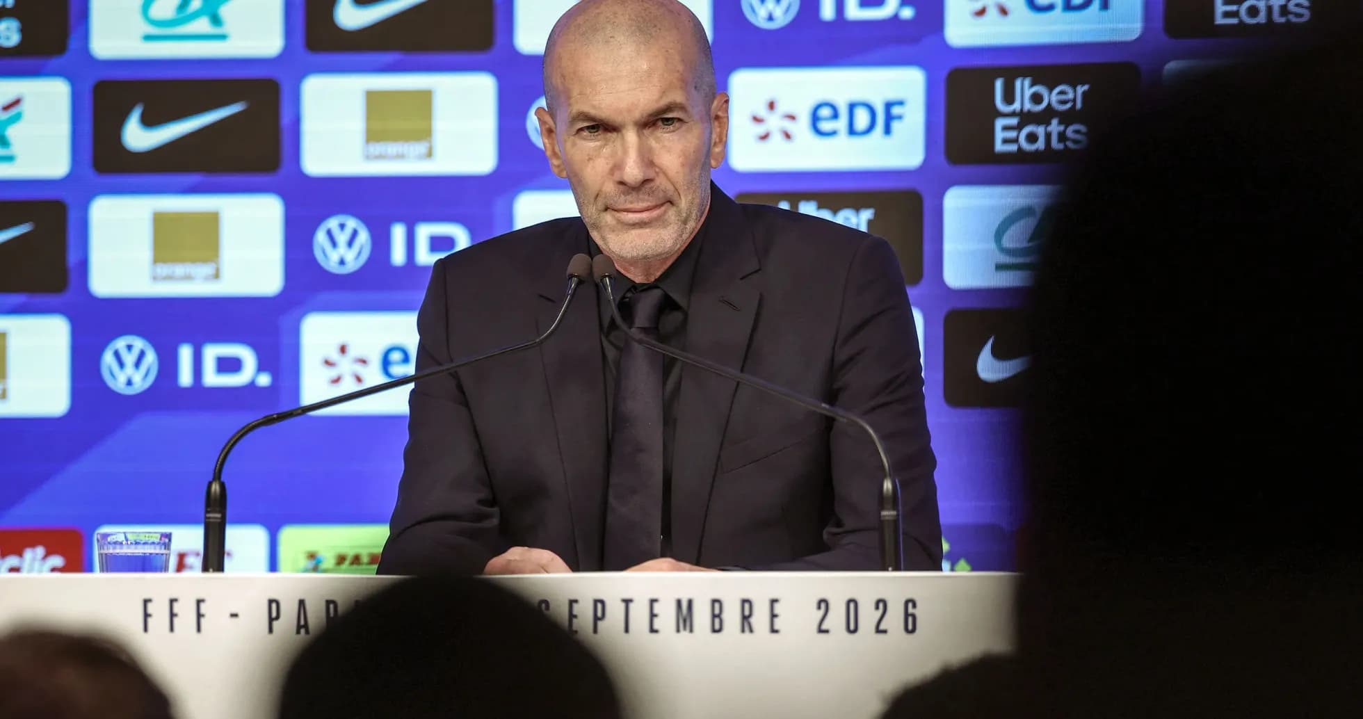 Entrenador en conferencia de prensa con logos detrás