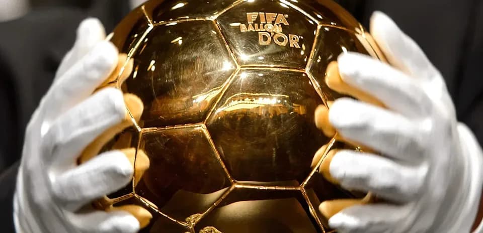 Balón de Oro sostenido por manos con guantes
