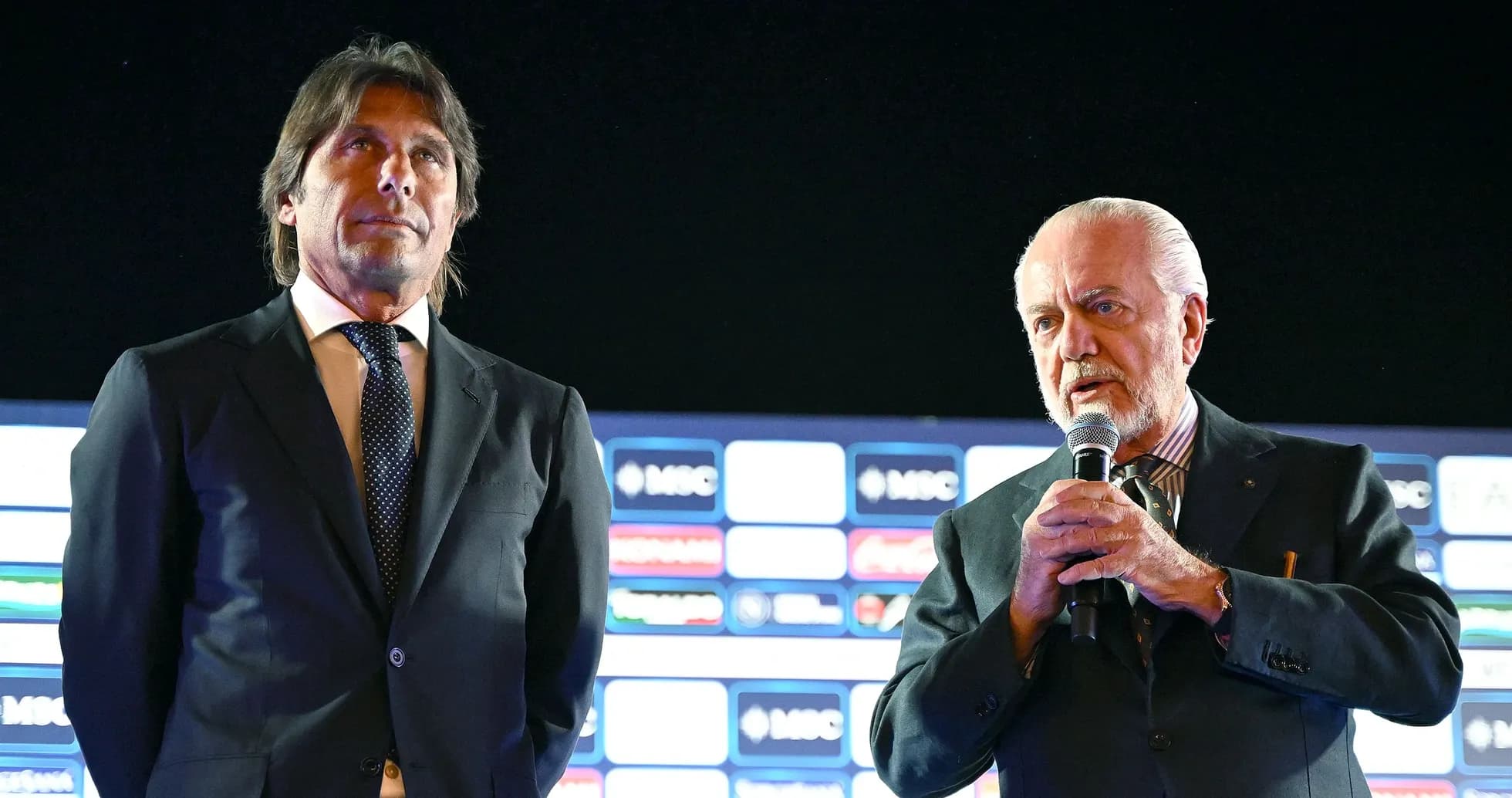 Dos hombres en un evento con micrófono y fondo gráfico