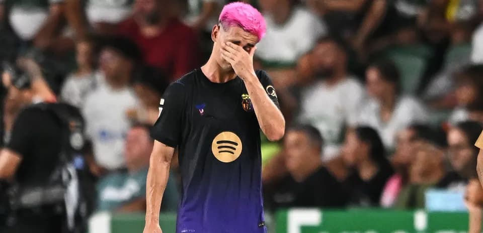 Jugador con cabello rosa se cubre la cara en el campo