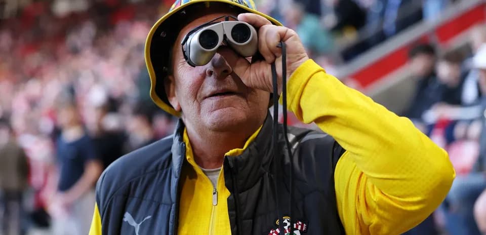 A fan wearing binoculars and a hat at the stadium