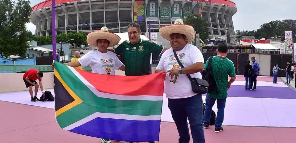 Aficionados sosteniendo bandera sudafricana frente al estadio