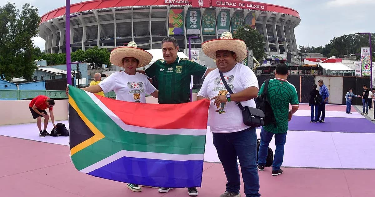 Aficionados sosteniendo bandera sudafricana frente al estadio
