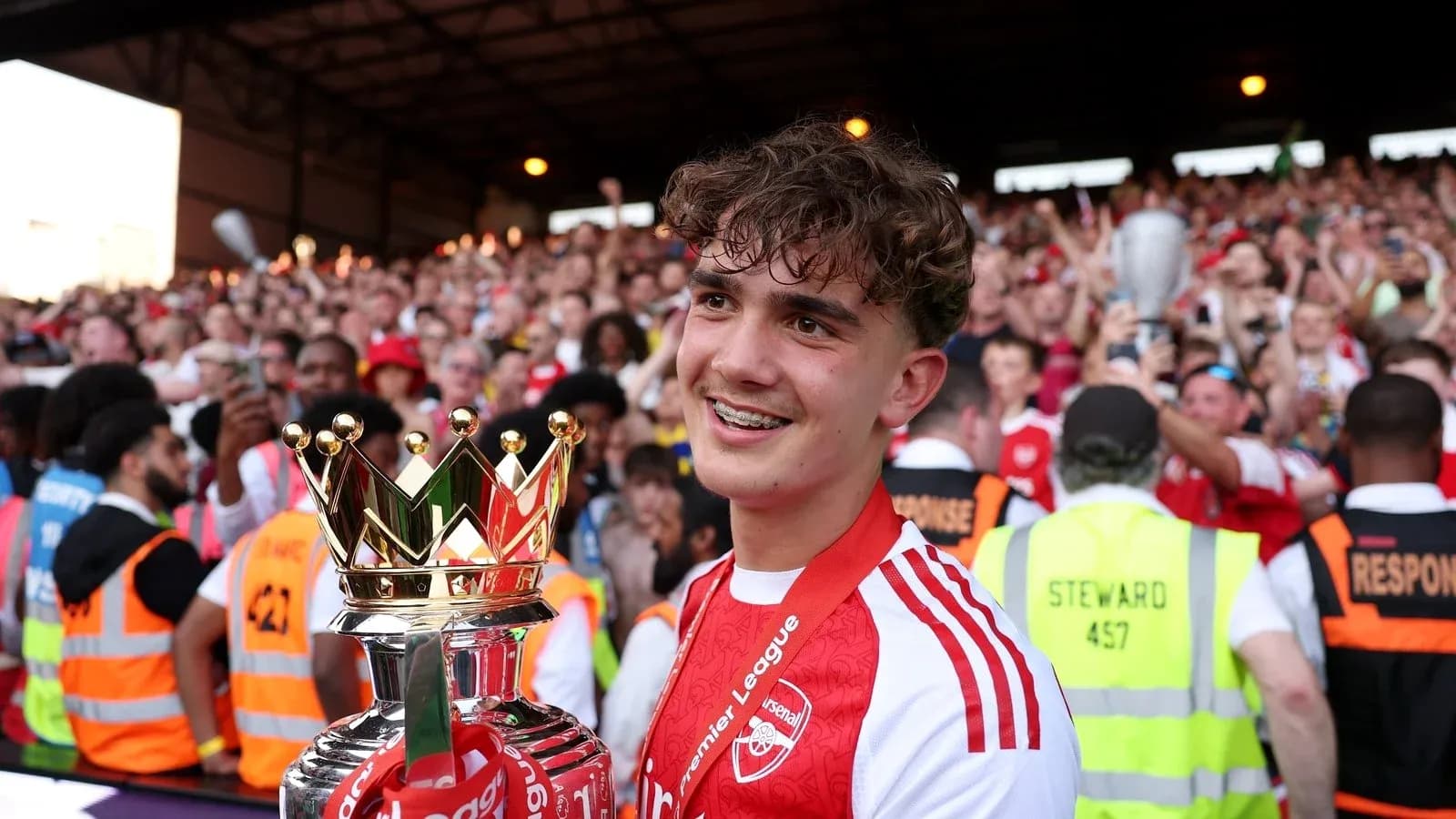 Jugador sosteniendo trofeo de la Premier League con aficionados