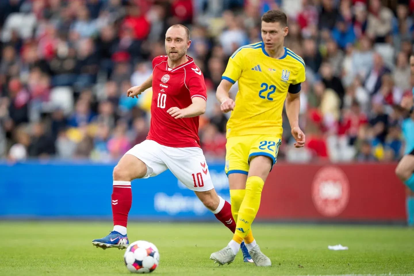 Jugador danés 10 corriendo con balón, jugador ucraniano 22 persiguiéndolo Jugador danés 10 corriendo con balón, jugador ucraniano 22 persiguiéndolo