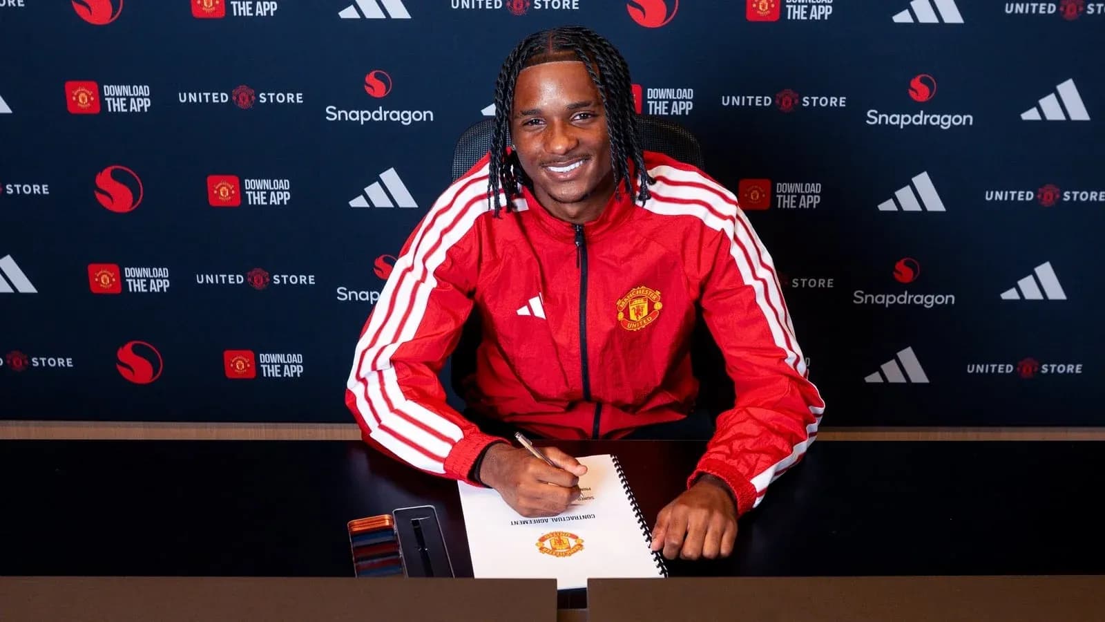 Jugador firmando contrato en mesa con logotipo de Manchester United Jugador firmando contrato en mesa con logotipo de Manchester United